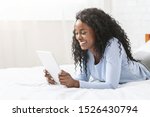 Interesting content. Millennial african girl reading blog on digital tablet lying in bed, free space