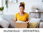 Excited african american girl unboxing cardboard delivery package, sitting at home, copy space