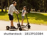 Bonding Concept. Father having ride on e-scooter with his cheerful son on the road in park, free space