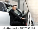 Successful middle-aged entrepreneur getting in expensive car, driving to airport, side view. Smiling bearded businessman sitting in car, going to business meeting or conference, empty space