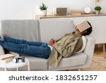 Remote education concept. Bored black teen student with book on his face sleeping on couch at home. African American teenager unwilling to do dull home assignment, napping on sofa with textbook