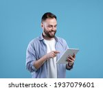 Joyful bearded man using tablet computer for online work or studies on blue studio background