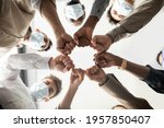 Small photo of Success And Teamwork Concept. Below view of young diverse group of business people in protective medical masks making fist bump standing in circle. Workers do fist pump together celebrating good deal
