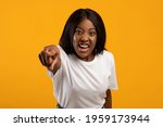 Small photo of Angry black lady yelling and pointing at camera, yellow studio background, closeup portrait. Furious african american young woman shrieking, feeling irritated. Negative emotions, anger concept