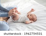 Caring Mother Making Gymnastics To Her Newborn Baby On Bed At Home, Unrecognizable Woman Helping Infant Kid To Relief Gas, Doing Exercises With Little Kid To Prevent Child Constipation, Cropped Image
