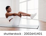 Bodyweight Workout Routine. Smiling young African American sportswoman doing v-ups abs exercises on floor yoga mat, doing crunches or sit-ups with raised legs and outstreched arms, working on six-pack