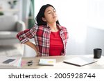 Small photo of Beautiful Young Asian Woman Suffering From Backache While Sitting At Desk In Home Office, Tired Korean Freelancer Lady Having Acute Lower Back Pain After Long Time Working With Laptop Computer