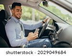 Bad driving habits, unsafe driving, driving and gadgets concept. Cheerful arab man entrepreneur going to office by auto, using cellphone while driving car, chatting with someone, side view, copy space