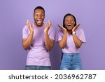 Wow. Portrait of overjoyed young black man and woman with open mouth gesturing in amazement looking at camera. Emotional surprised couple posing standing isolated over purple studio background wall