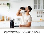 Small photo of Young Arab guy drinking protein shake from bottle at kitchen, copy space. Millennial Eastern man using meal replacement for weight loss, having sports supplement for muscle gain. Body care concept