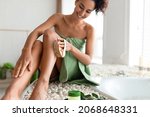Small photo of Young woman in towel making anti cellulite or lymphatic drainage massage near foamy bath at home, selective focus. Millennial lady dry brushing her leg, exfoliating skin, pampering herself in bathroom