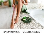 Small photo of Unrecognizable young woman shaving legs with razor, removing unwanted hair, making epilation sitting on bathtub at home, closeup. Depilation and bodycare, domestic spa concept