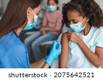 Kids Vaccination. Nurse Vaccinating Black Preteen Girl Injecting Vaccine Against Covid-19 With Syringe Indoors. Child Getting Vaccinated For Immunization In Modern Clinic. Selective Focus