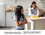 Small photo of Sad asian girl taking offence at her busy mother working online on laptop computer from home, free space. Child feeling neglected and lonely with her mom having remote job