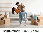 Small photo of Affectionate young Asian couple dancing in their house among cardboard boxes on moving day, full length. Happy millennial spouses having fun while relocating to new property, copy space