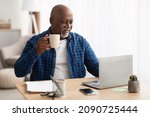 Small photo of African American Senior Businessman Drinking Coffee Using Laptop Computer Sitting During Break Holding Cup At Workplace In Office. Successful Entrepreneurship And Freelance Career In Older Age