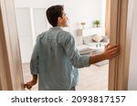 Small photo of Rear back view of excited young man walking in his apartment, entering new home, happy young guy standing in doorway of modern flat, looking at design interior, coming inside, selective focus