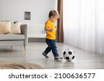 Small photo of Future champion. Adorable little toddler boy playing football, hitting ball at home, having fun in living room interior, copy space