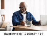 Small photo of Entrepreneurship Career. Mature African American Man Taking Notes Working Sitting At Laptop Computer In Modern Office Indoors. Senior Businessman Writing Report At Workplace, Wearing Eyeglasses