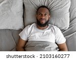Small photo of Depression Concept. Above top view portrait of upset black man lying in bed in the morning and thinking, looking up. Sad black male feeling lonely or stressed, suffering from lack of sleep, distraught