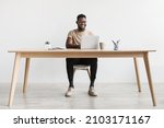 Small photo of Happy young black man using laptop computer for online work at table in home office, free space. Cool African American guy having remote job, freelancing on web. Modern business concept