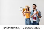Small photo of Young travellers couple with megaphone announcing excited deals for tourists, woman holding loudspeaker and pointing at free space, man holding passports and tickets, light background, panorama