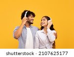 Small photo of Loving indian couple in headphones listening to music, hugging and looking at each other over yellow studio background. Excited lady enjoying favorite sountracks with her boyfriend
