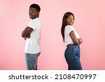 Side view of African American young couple standing separate back to back on pink studio wall. Profile portrait of black man and woman don't talk to each other after family quarrel, crossing arms