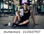Small photo of Young Arab Male Athlete Relaxing On Floor After Training At Gym, Smiling Middle Eastern Man Resting Next To Blank Container With Supplement Pills, Enjoying Bodybuilding And Healthy Lifestyle