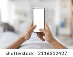 Mobile Mockup. Unrecognizable Male Holding Blank Smartphone With White Screen While Relaxing In Bed At Home, Man Using Empty Mobile Phone With Copy Space For App Or Website Design, POV Shot