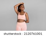 Portrait of happy young black woman in sports outfit posing and smiling on grey studio background. Fit millennial African American female being in great shape, leading active lifestyle