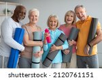 Small photo of Group of active athletic pensioneers different nationalities in sportrswear attending yoga class at retreat center, holding fitness mats and cheerfully smiling at camera. Sport for senior people