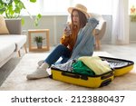 Small photo of Terrified young woman reading shocking travel news or negative message about tourism on smartphone while packing suitcase at home. Cancelled flight, traveling problems during covid epidemic