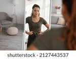 Weight Gain. Displeased Fit Woman Touching Fat Belly Looking In Mirror Standing At Home, Struggling To Lose Excess Weight After Unsuccessful Diet And Slimming. Selective Focus
