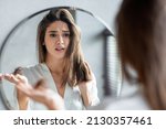Small photo of Portrait of stressed young woman with bunch of fallen hair in hand looking at mirror in bathroom, scared upset millennial lady in white silk robe suffering hairloss problem, selective focus