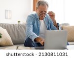 Small photo of Poor Eyesight. Senior Man Squinting Eyes Using Laptop Wearing Eyeglasses Having Problems With Vision Sitting On Couch. Ophtalmic Issue, Bad Sight In Older Age, Macular Degeneration Concept