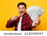 Small photo of Portrait Of Excited Man Holding Fan Of Money Cash In Hands Pointing Finger Showing It To Camera On Yellow Orange Background. Guy Posing With Banknotes. Financial Success And Currency Concept. Big Luck