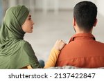 Small photo of Marital Crisis. Unhappy Middle Eastern Wife Touching Husband's Shoulder While He Ignoring Her Sitting Back To Camera At Home. Marriage And Relationship Issues Concept