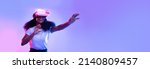 Small photo of Excited young African American lady using VR glasses, touching something invisible at copy space, millennial female experiencing ar virtual reality adventure on neon studio background, panorama banner