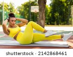 Small photo of Weight Loss Concept. Confident Sportive Young Black Woman Doing Side Bicycle Crunches Bringing Elbow Toward Knee With Raised Leg On Yoga Mat, Training Outside At Court. Pilates And Warm Up Concept