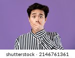 Oh No. Closeup portrait of surprised amazed Asian man covering mout with hand palm looking staring at camera, shocked by news, standing isolated on purple violet studio background wall