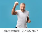 Small photo of Overjoyed senior man screaming in excitement, gesturing yes shaking clenched fists on blue studio background. Triumphant elderly male celebrating his success, cheering favorite team at competition