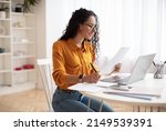 Small photo of Middle Eastern Lady Holding Paper And Using Laptop Computer Making Business Report Working Online Sitting At Workplace In Modern Office. Successful Business Accounting And Entrepreneurship