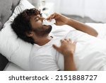 Seasonal virus, coronavirus, flu, allergy concept. Closeup photo of sick indian millennial guy blowing his nose, lying in bed with fever, side view, copy space, home interior