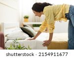 Portrait of cheerful young woman making bed after wake up feeling rested, happy lady changing clean bedsheets at home standing in modern bedroom. Domestic chores and household concept