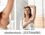 Small photo of Attractive Woman Applying Antiperspirant Underarms For Sweat Protection Standing Raising Arm Posing In Modern Bathroom At Home. Armpits Skin Care And Hygiene Routine Concept