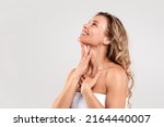 Double Chin Treatment. Beautiful Middle Aged Woman Touching Soft Smooth Skin On Neck, Attractive Mature Lady Standing Wrapped In Towel Over Light Grey Background, Enjoying Her Beauty, Copy Space