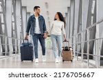Small photo of Happy Travellers. Portrait Of Young Arab Couple Walking With Suitcases At Airport, Romantic Middle Eastern Spouses Carrying Luggage And Smiling To Each Other While Going To Departure Gate, Free Space
