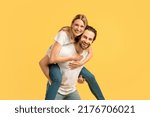Glad smiling millennial caucasian woman on man on back in white t-shirt, enjoy moment, have fun at free time, isolated on yellow background, empty space. Ad and offer, couple relationship and love
