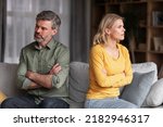 Small photo of Crisis In Relations. Middle Aged Husband And Wife Offending To Each Other After Argue, Grumpy Spouses Sitting On Couch With Folded Arms, Married Couple Angry After Domestic Quarrel, Free Space